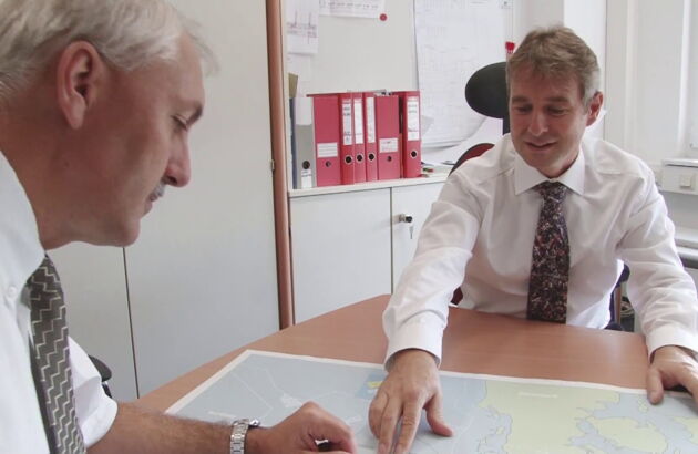 Two men sit in the office and look at a world map.